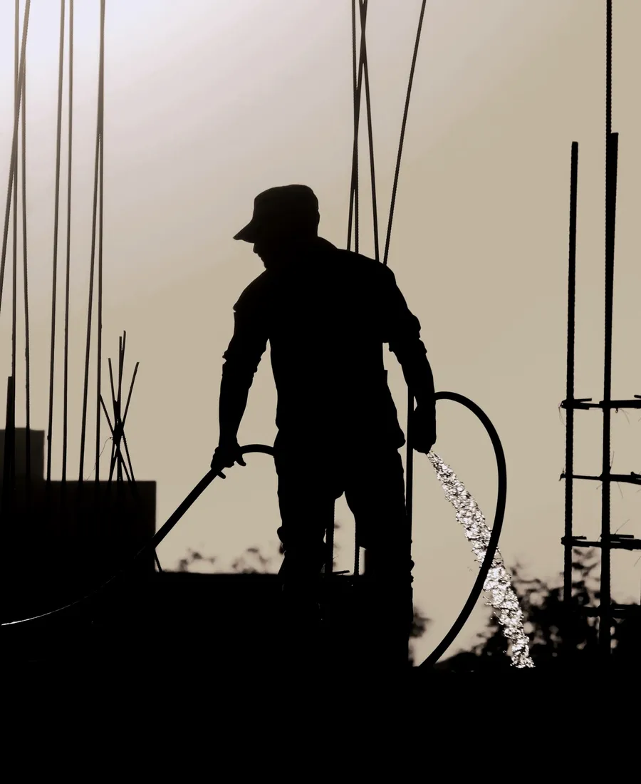 Bauarbeiter beim Betonieren auf einer Baustelle, Silhouette gegen den Abendhimmel